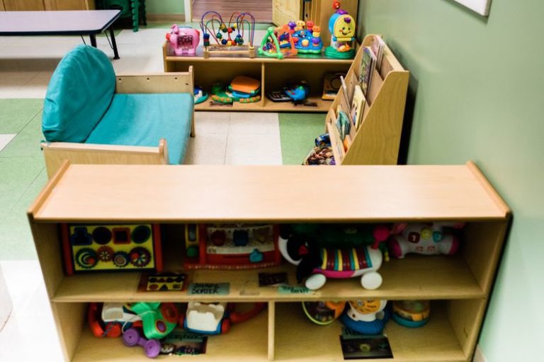 Aquamarine colored sofa and cabinets with reading materials and full of toys Smiling cute little baby wearing pink pajamas at a Christian Preschool & Daycare Serving Branford & Wallingford, CT